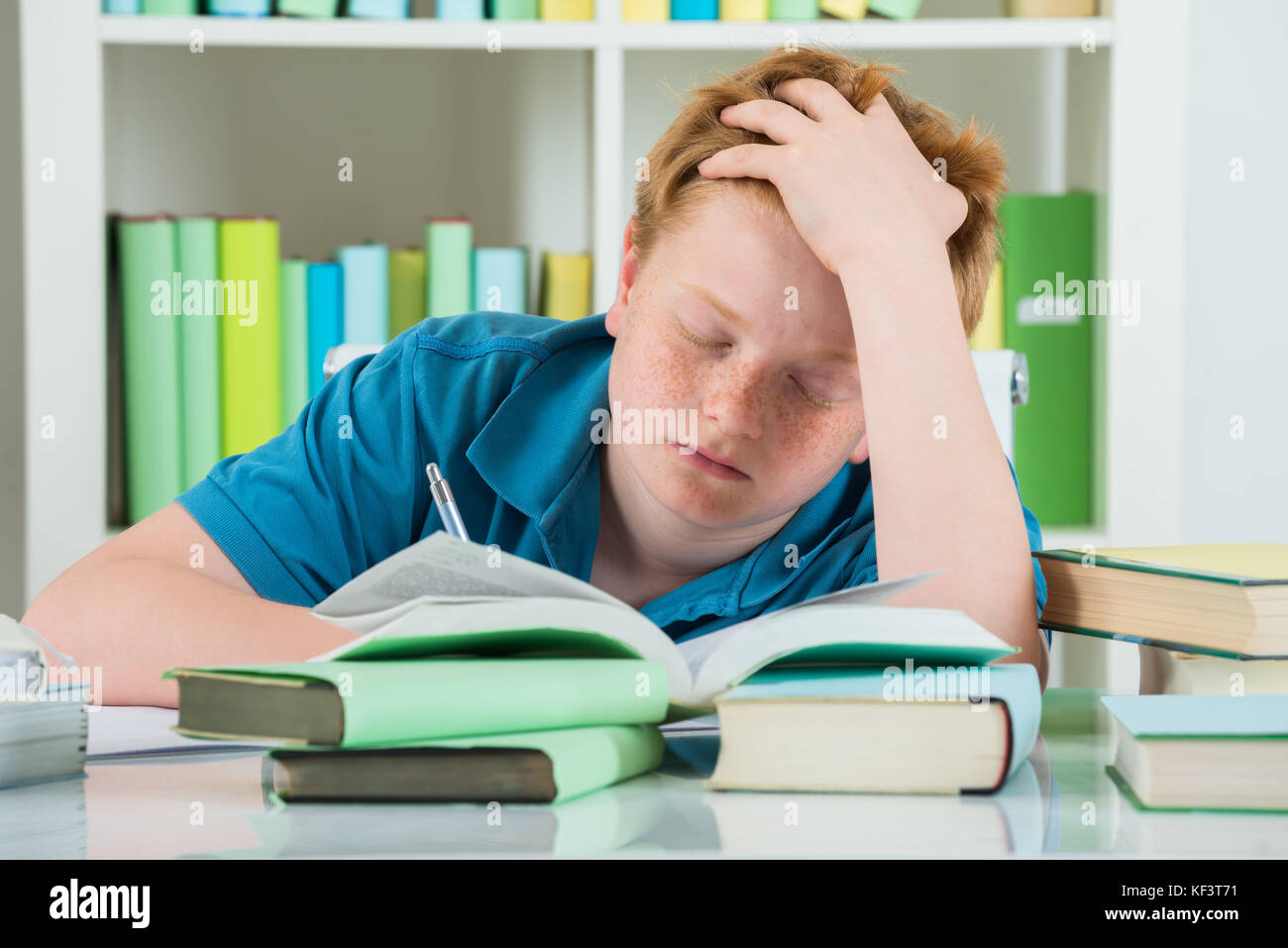 Erschöpft Junge Studieren in Bibliothek mit Büchern auf dem Schreibtisch Stockfoto