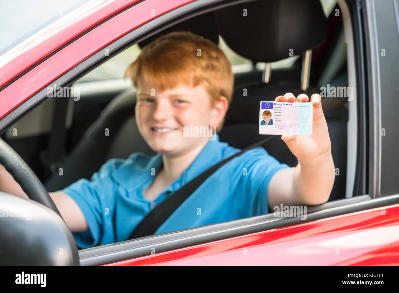 Lächelnde Junge sitzt im Auto, Führerschein Stockfoto