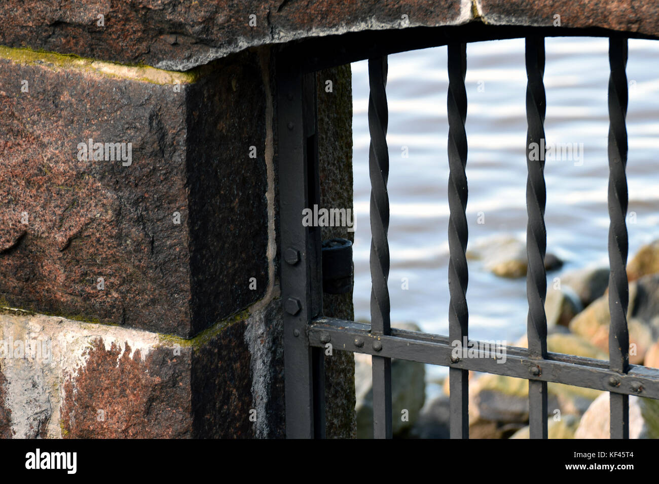 Nahaufnahme der alten Gefängnis bars und Steinmauer. außerhalb der Zelle steinig ist der Strand und das Meer. Stockfoto