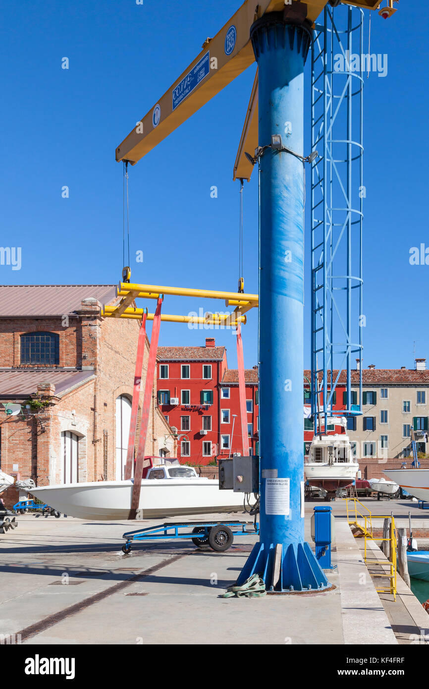 Kleines Boot ausgesetzt in der Luft in einer Schlinge auf dem Boot Abheben beim Start in die Werft auf der Insel Giudecca, Venedig, Italien. Die Boote sind in trocken gehalten Stockfoto