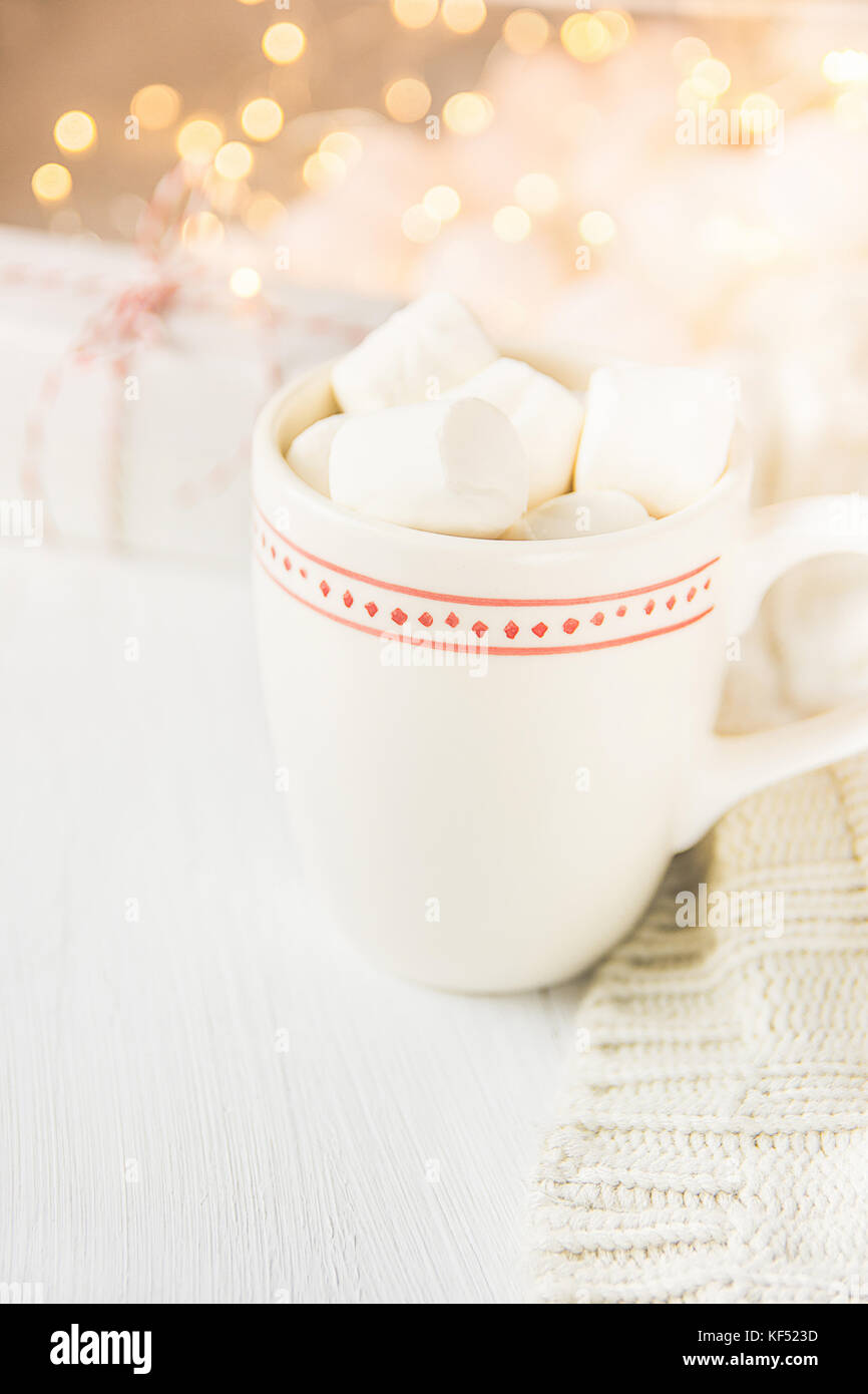 Weiße Tasse mit heißer Schokolade Kakao trinken und Marshmallows auf. Sekt Girlande Lichter im Hintergrund. strickpullover Geschenkbox. weichen Pastellfarben Stockfoto