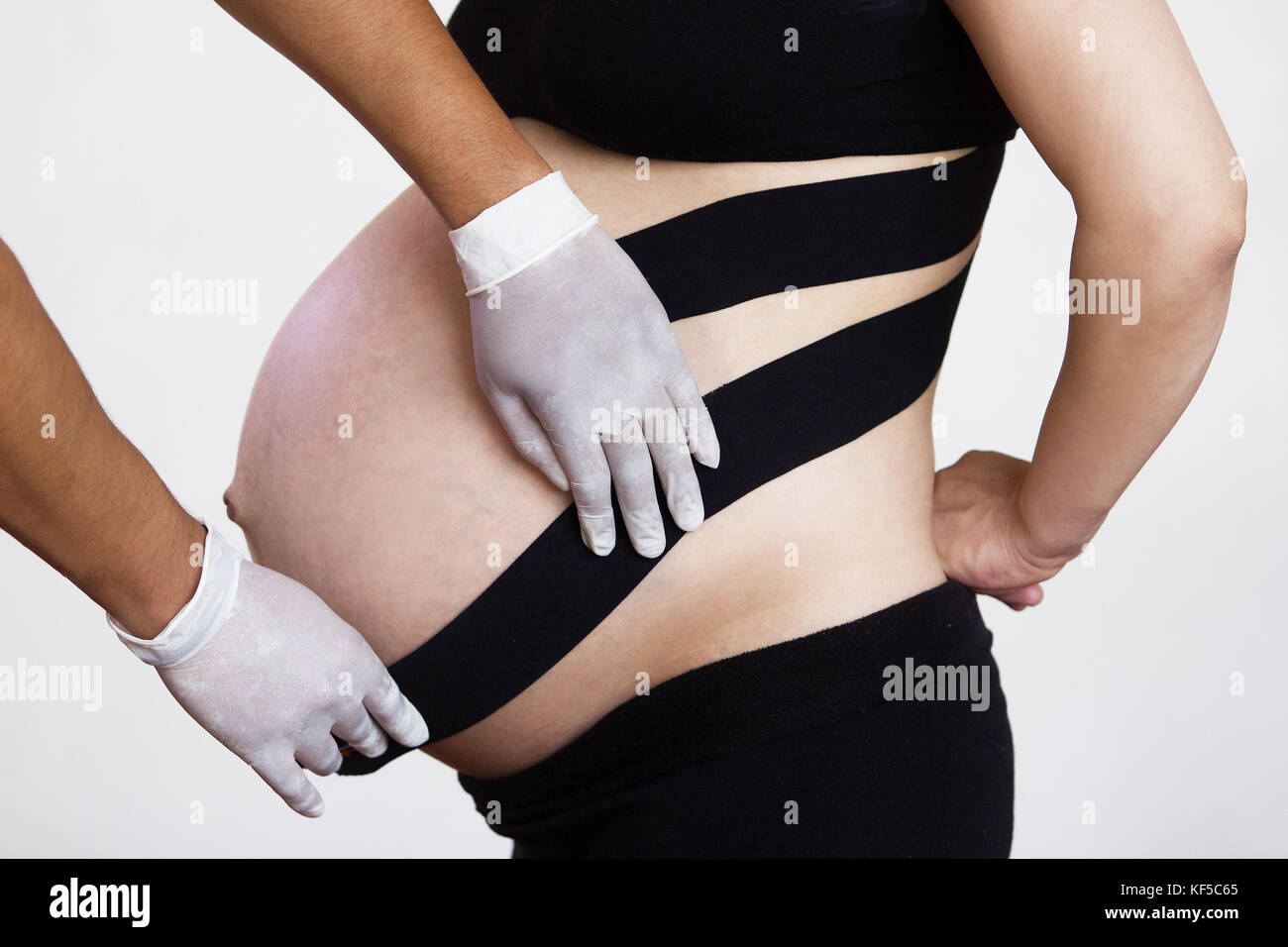 Arzt Physiotherapeut mit Handschuhen Anwendung Kinesiotaping auf dem Bauch einer schwangeren Frau zu Rückenschmerzen verringern Stockfoto