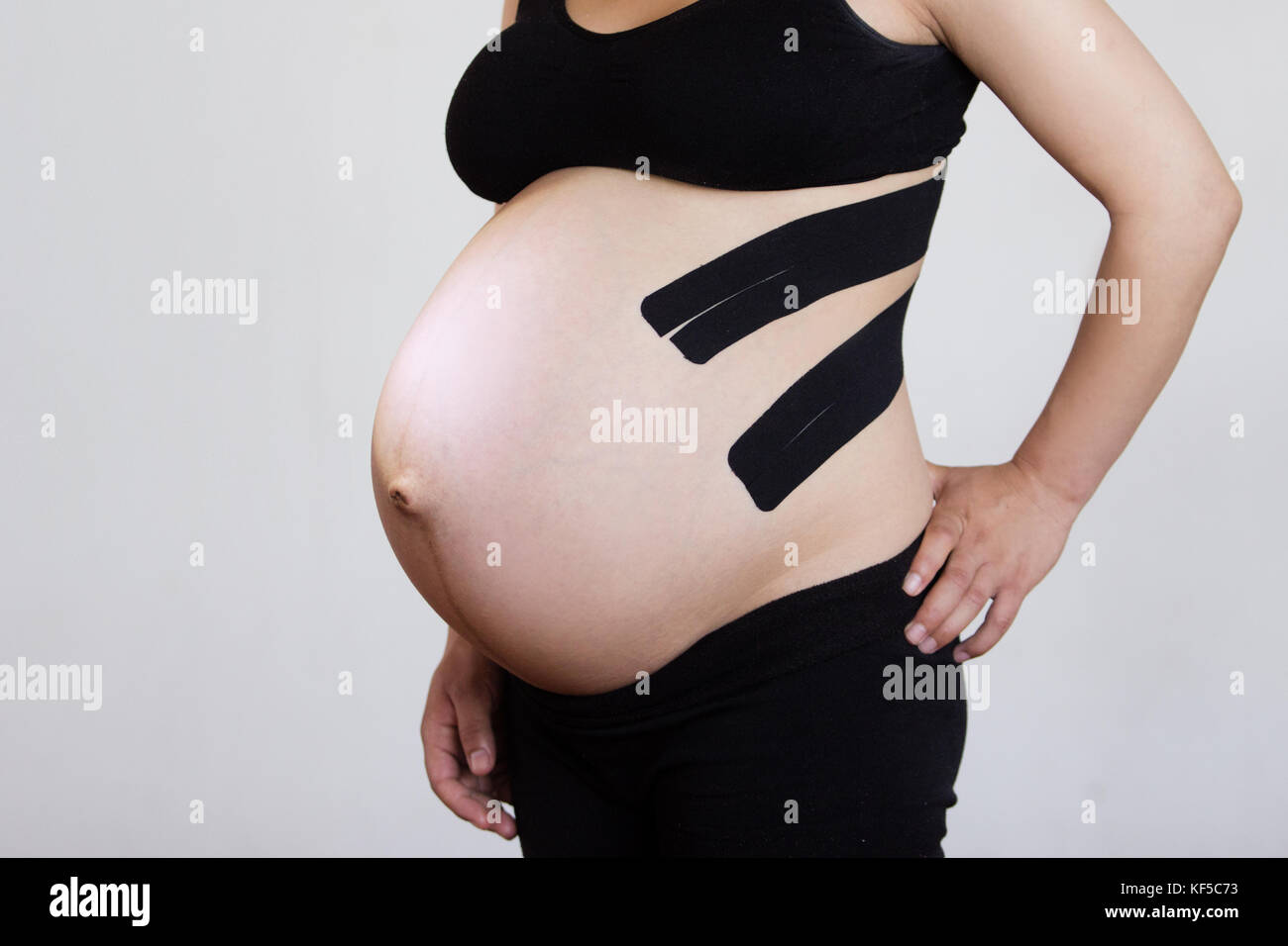 Eine schwangere Frau mit zwei Streifen von Kinesiotaping auf dem Rücken Rückenschmerzen verringern Stockfoto