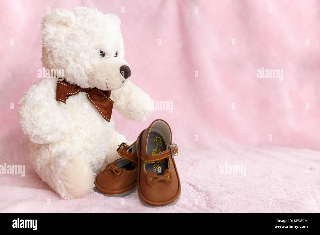 Teddy Bear mit Paar von Mary Jane style Baby Schuhe gegen eine blass rosa Hintergrund. Stockfoto