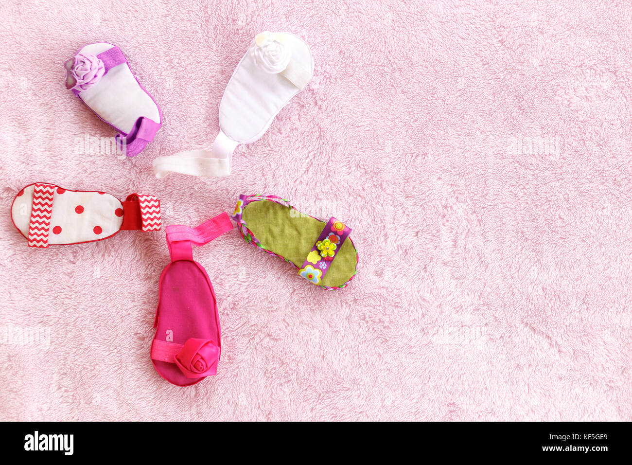 Fünf baby Sandalen verschiedener Farben in eine kreisförmige Form gegen eine blass rosa Hintergrund angeordnet Stockfoto