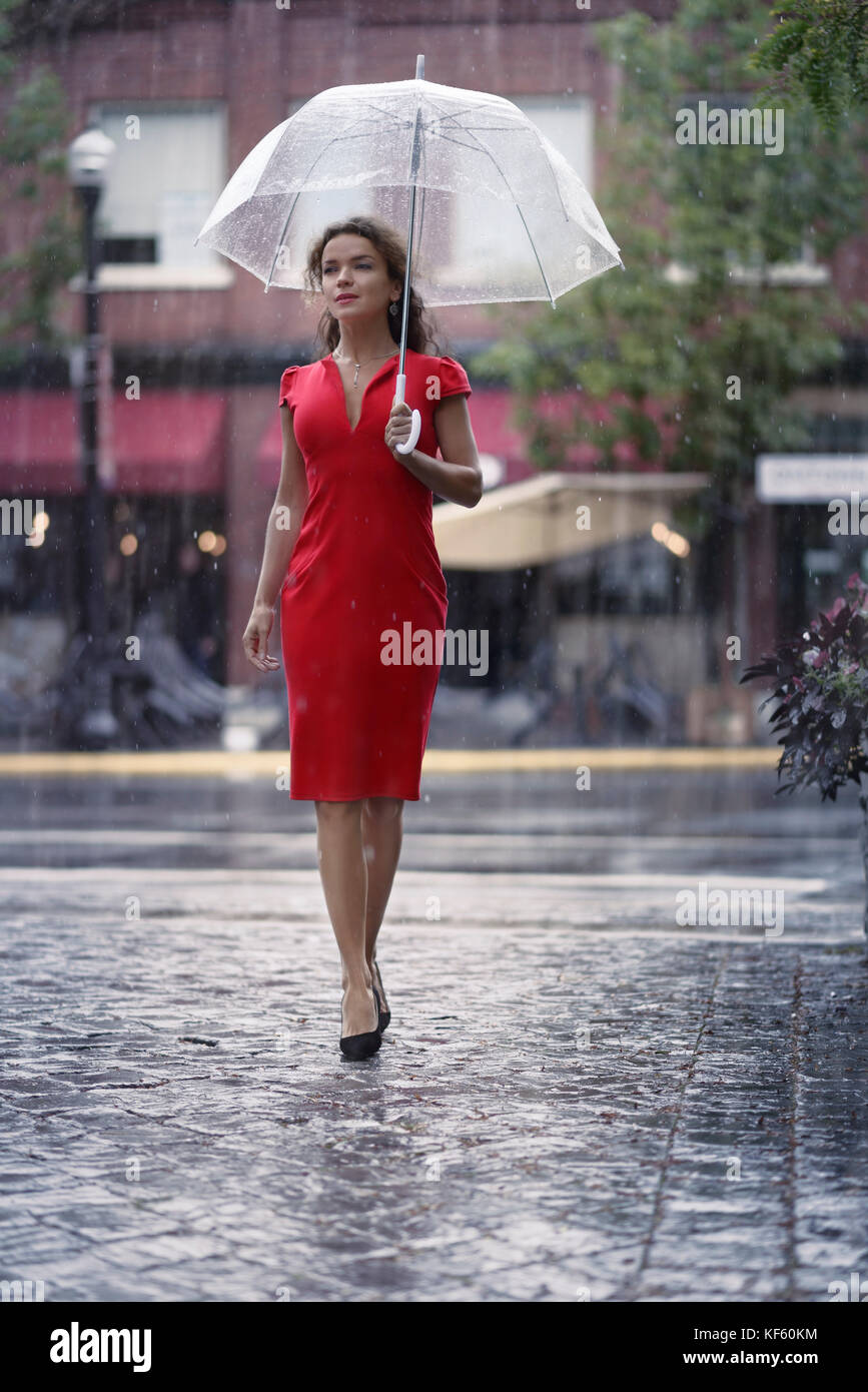 Junge Frau in einem roten elegantes Kleid mit einem Regenschirm Wandern an  einem regnerischen Tag auf einer Straße der Stadt Stockfotografie - Alamy