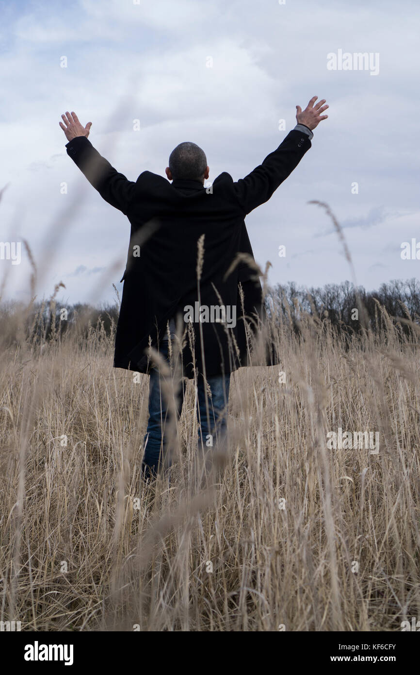 Ansicht der Rückseite ein Mann mit einem Mantel steht ein Feld ausgestreckten Armen Stockfoto