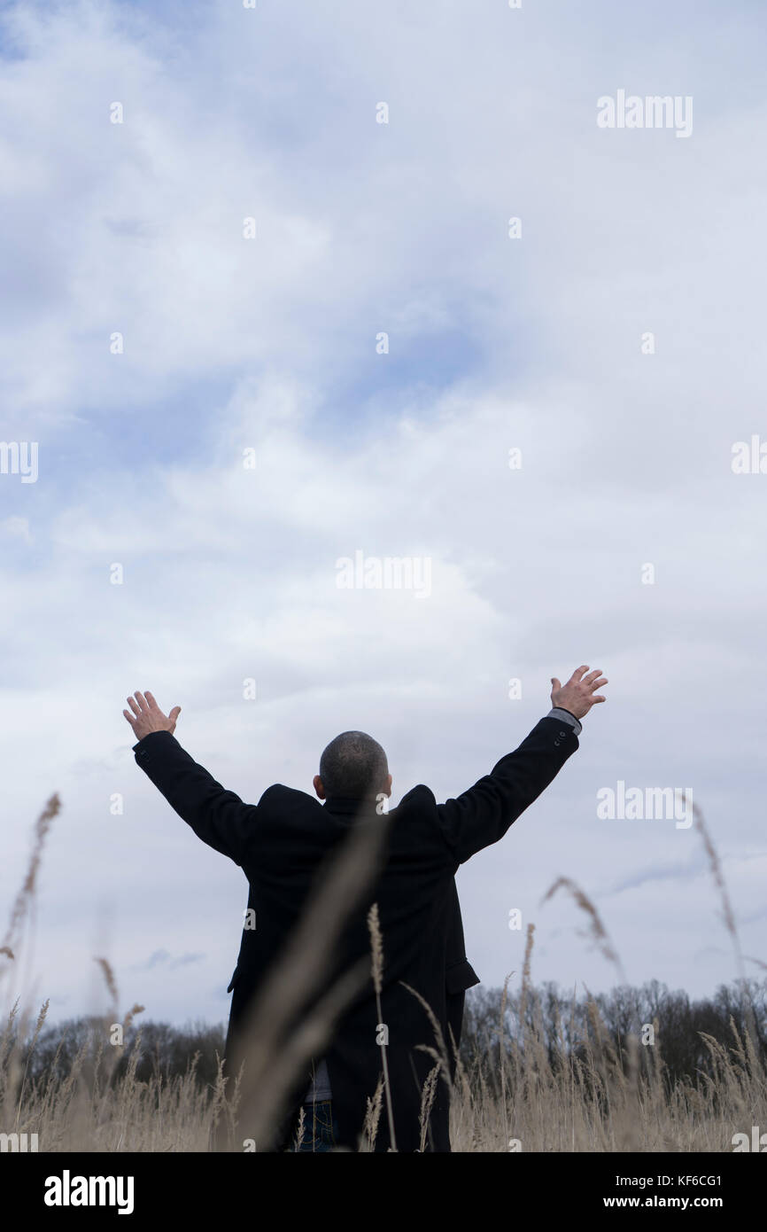 Ansicht der Rückseite ein Mann mit einem Mantel steht ein Feld ausgestreckten Armen Stockfoto