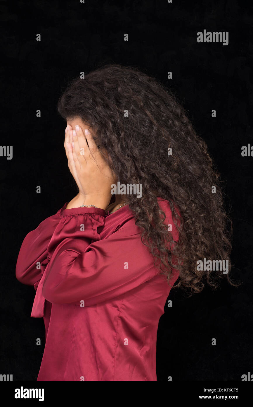 Porträt einer jungen Frau verstecken Gesicht mit den Händen vor einem schwarzen Hintergrund Stockfoto