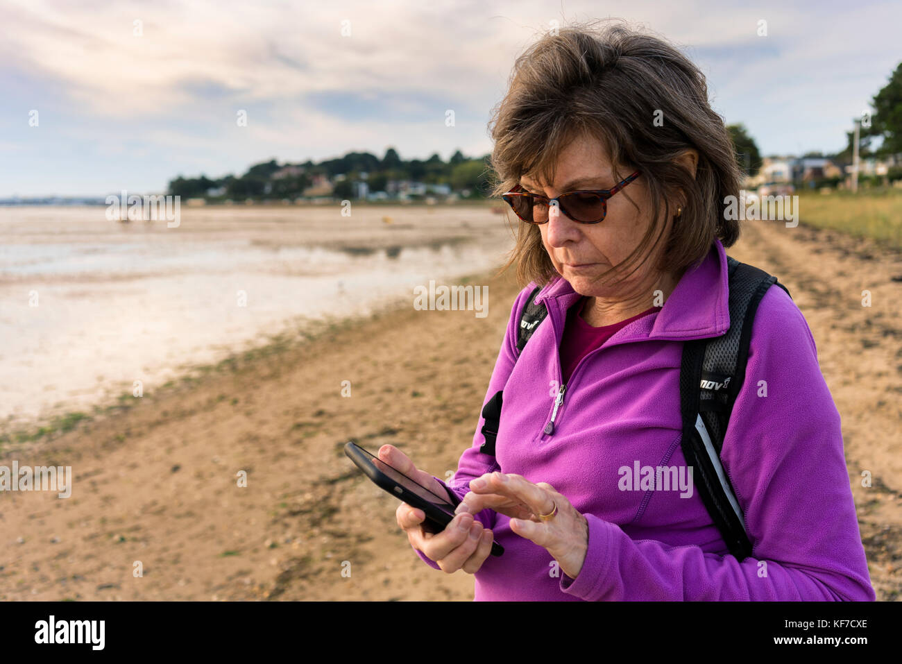65 Jahre alte Dame texting, stehend auf einem Strand. Stockfoto