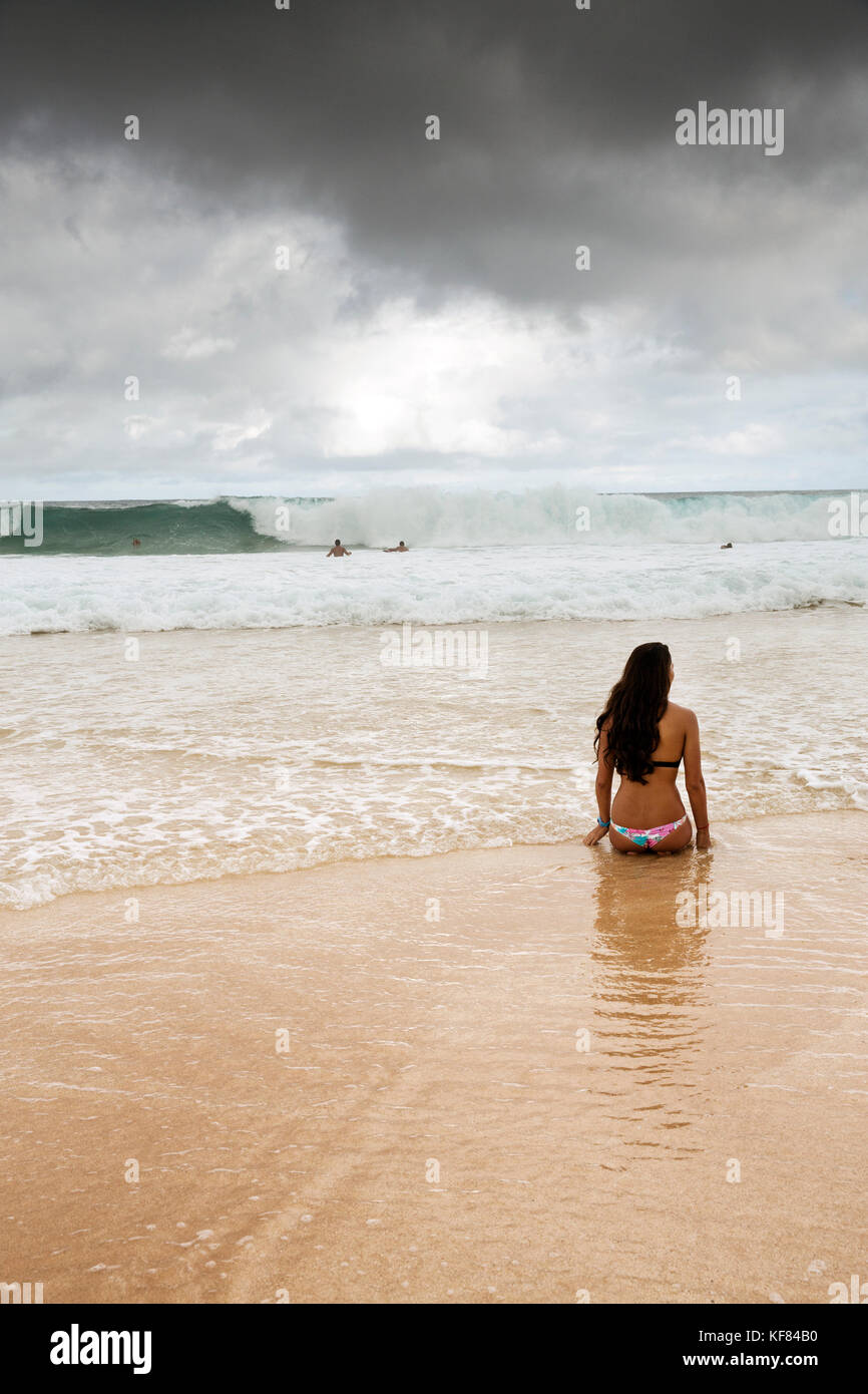 Usa, Oahu, Hawaii, Logan garcia sitzt am Strand am Rand der Brandung am Pipeline Beach an der Nordküste Stockfoto