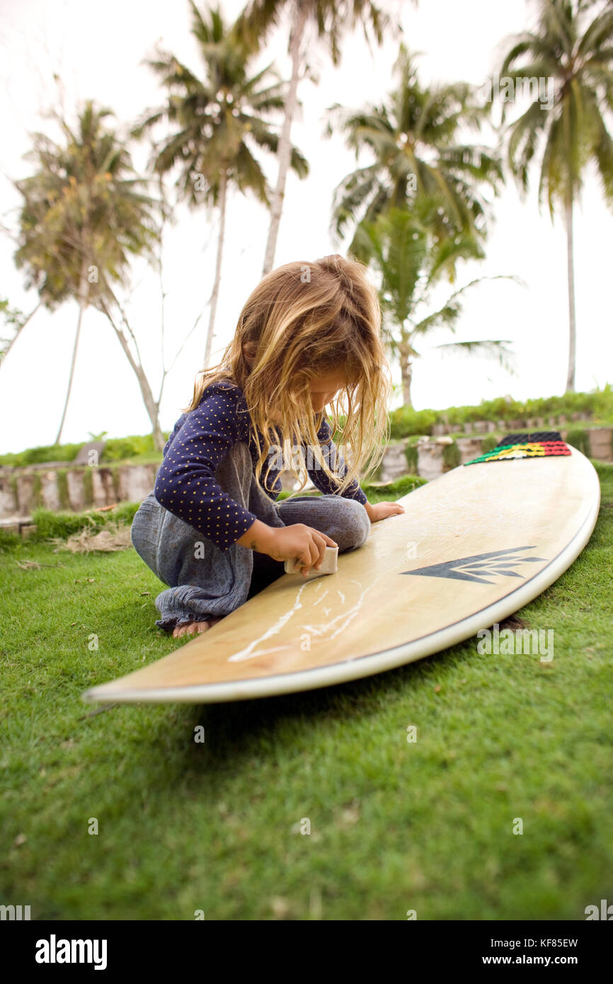 Indonesien, Mentawai Inseln, kandui Surf Resort, Mädchen wachsen Surfboard auf Rasen mit Palmen im Hintergrund Stockfoto