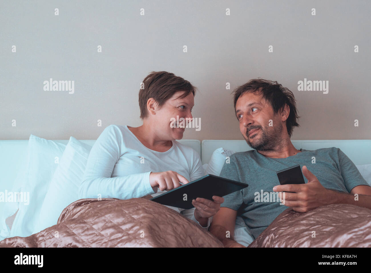 Glückliches Paar, Mann und Frau im Schlafzimmer über elektronische Geräte Stockfoto