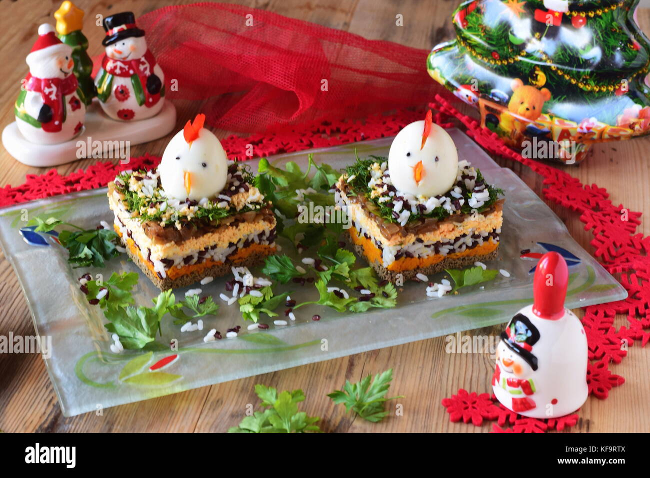 Salat in Schichten mit Hühnerleber, Zwiebeln, Karotten, schwarzer und weißer Reis, Petersilie und Dill mit Huhn den Kopf von gekochten Eiern dekoriert Stockfoto