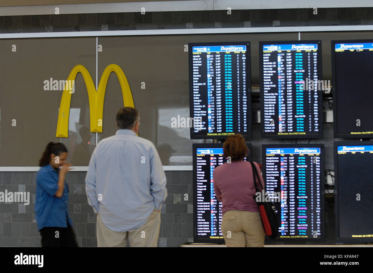 Passagiere auf dem Flug - Informationen Abflüge Bildschirme neben einem McDonald's Restaurant Logo im TerminalC Stockfoto