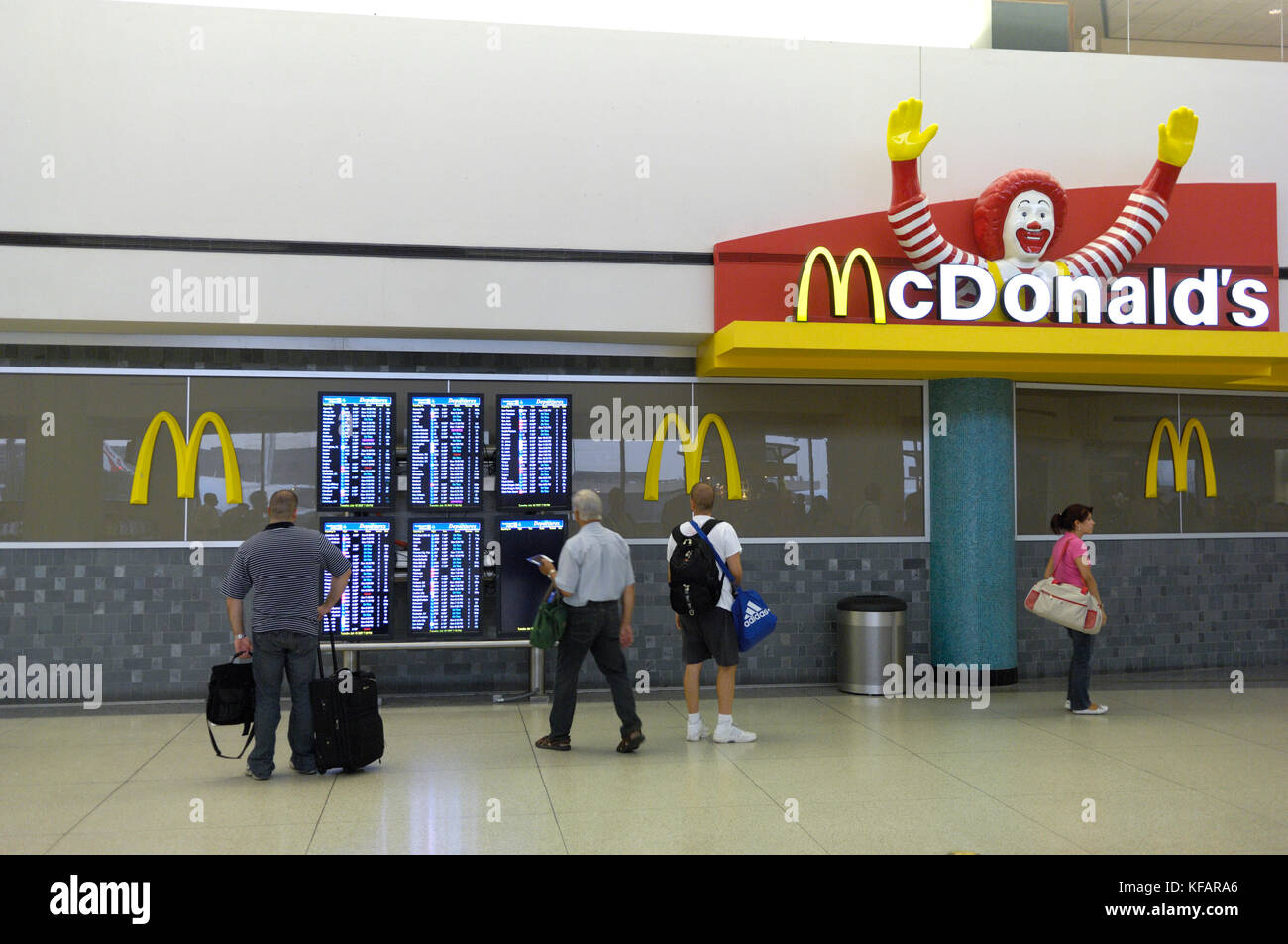 Passagiere mit Gepäck auf dem Flug Informationen Bildschirme neben Mcdonald's in der TerminalC Stockfoto