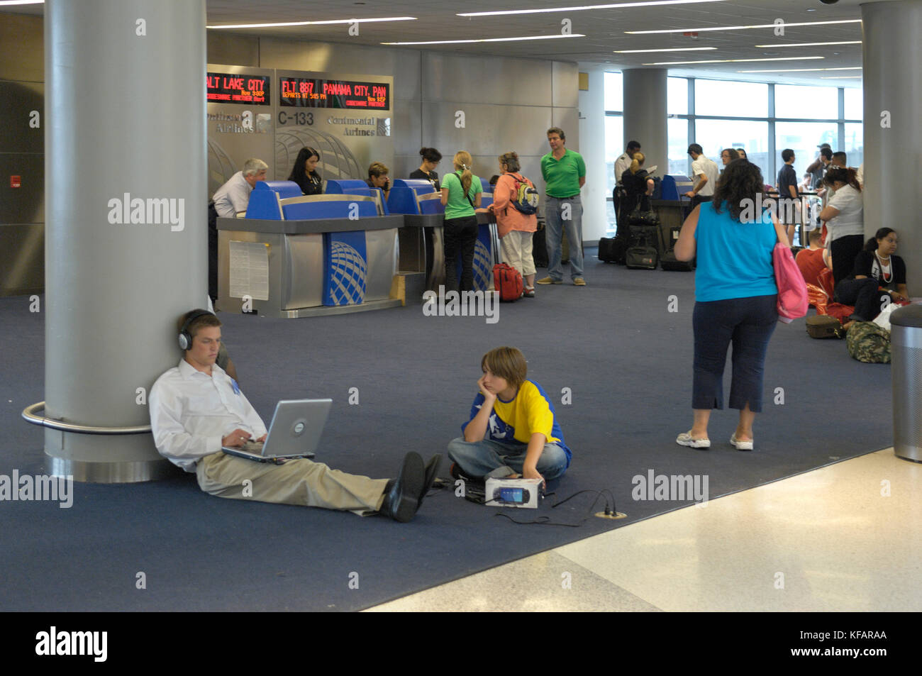 Mann und ein Junge sitzt auf dem Boden mit einem Laptop mit Continental Airlines gate Check-in-Schalter hinter dem TerminalC Stockfoto