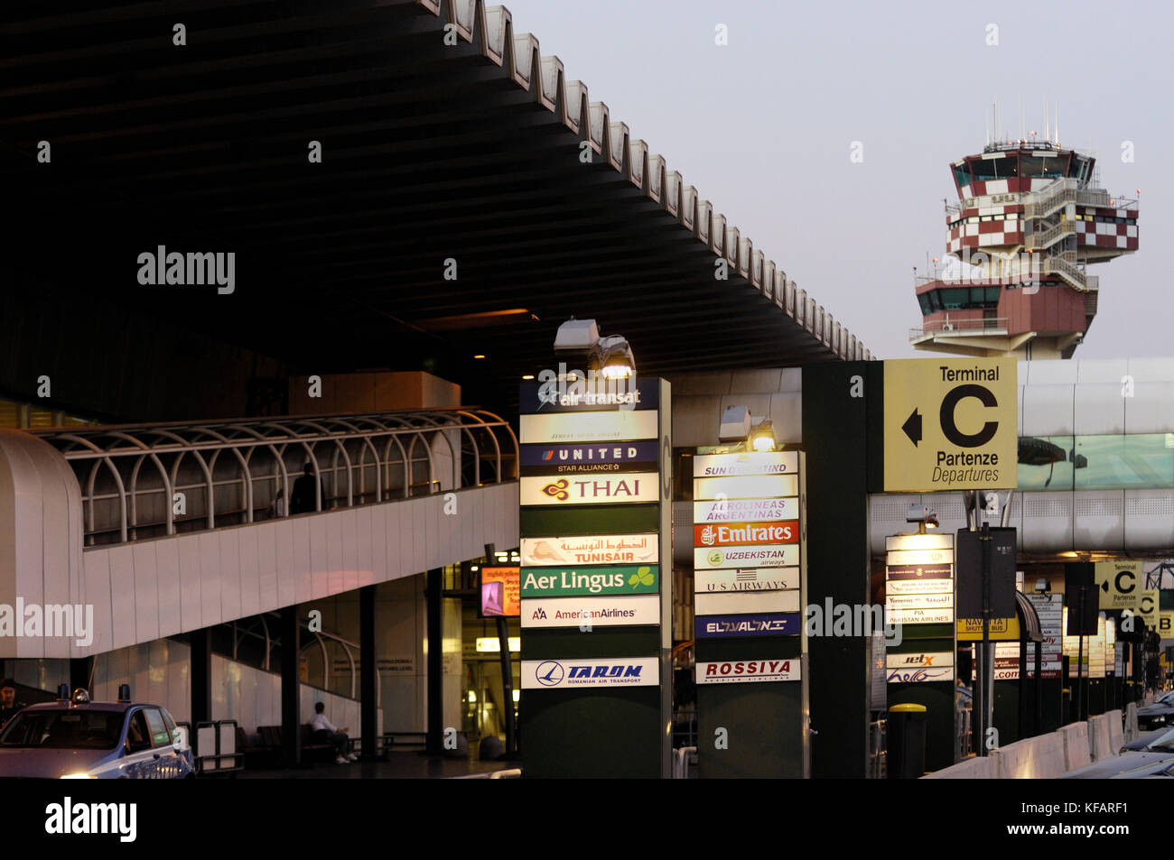 Anzeichen für Airlines, Klemmeb und TerminalC in englischer und italienischer Sprache mit dem Terminal und der Luftverkehrskontrolle - Tower hinter Stockfoto