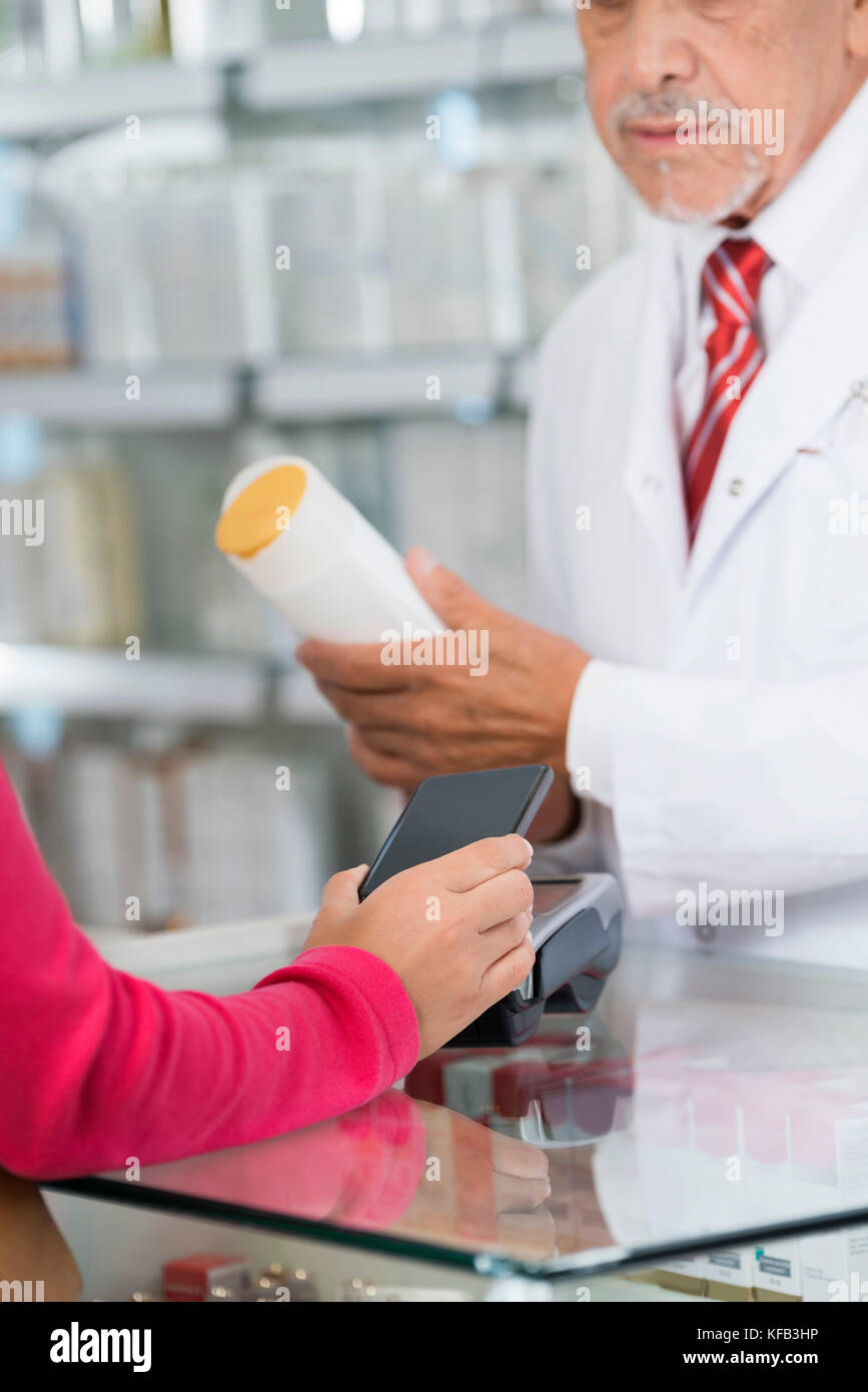 Frau, die NFC-Zahlung während Chemiker holding Shampoo Flasche Stockfoto