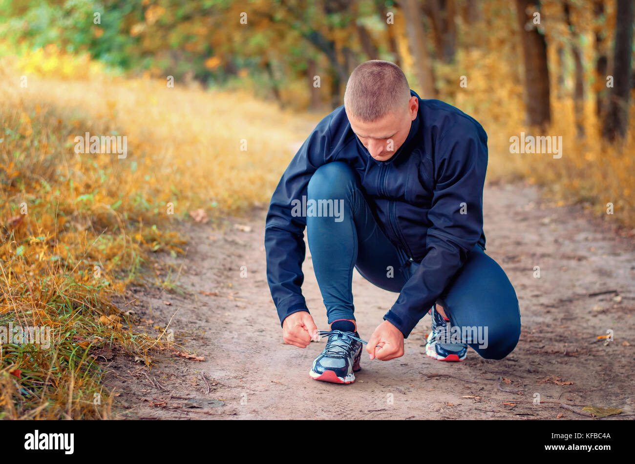 Eine junge fitness Athleten in einem schwarzen Sport Leggins und Sneakers Schnürsenkel bindet auf einem Pfad auf der gelben Herbst Wald. Stockfoto