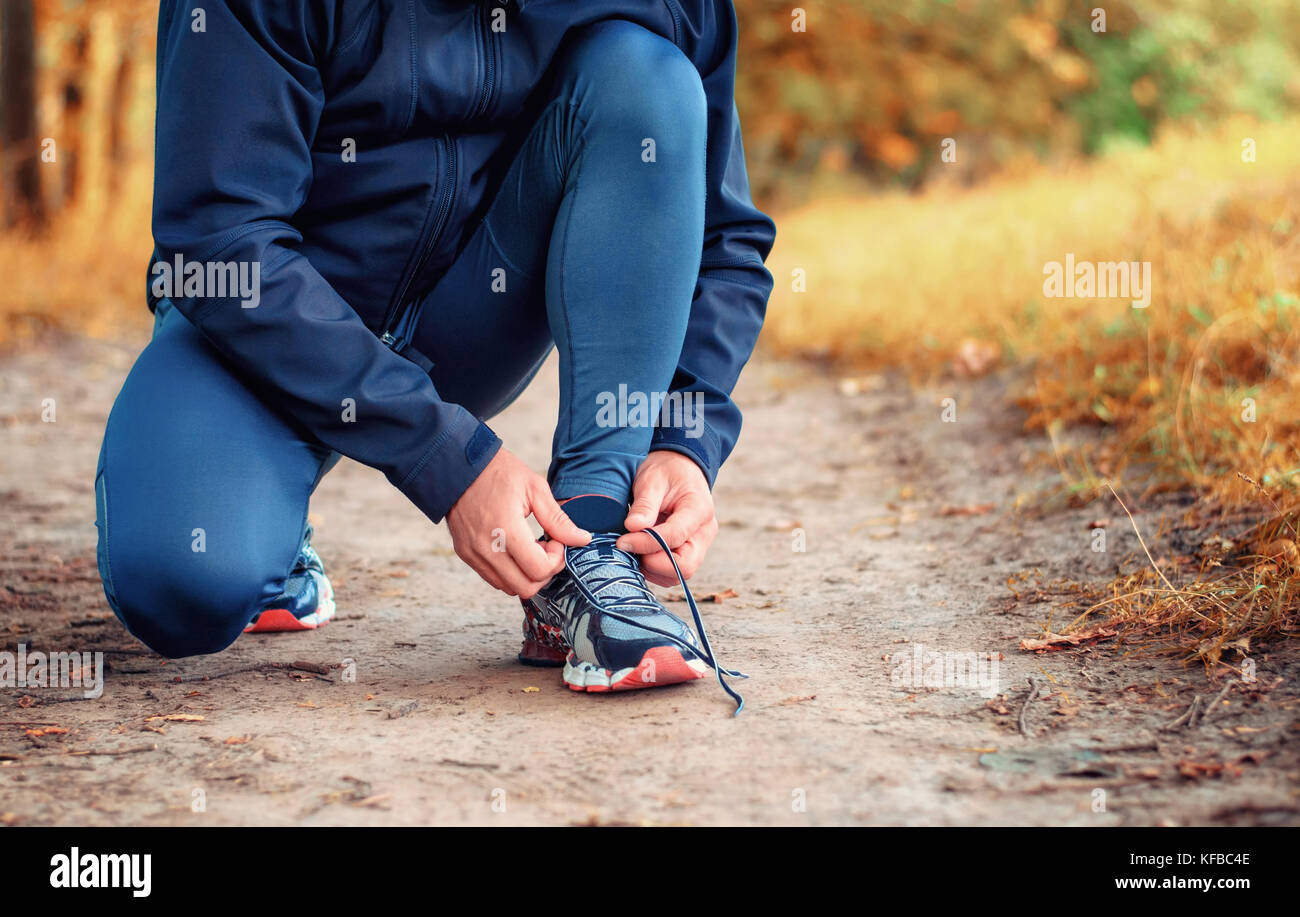 Nahaufnahme einer Beine der Läufer in einem schwarzen Sport Leggins und Sneakers Schnürsenkel bindet auf einem Pfad auf der gelben Herbst Wald. Stockfoto
