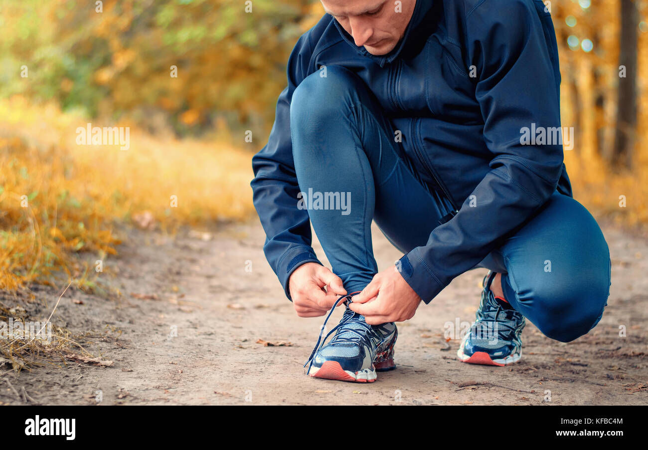 Eine junge schlanke Läufer in einem schwarzen Sport Leggins und Sneakers Schnürsenkel bindet auf einem Pfad auf der gelben Herbst Wald. Stockfoto