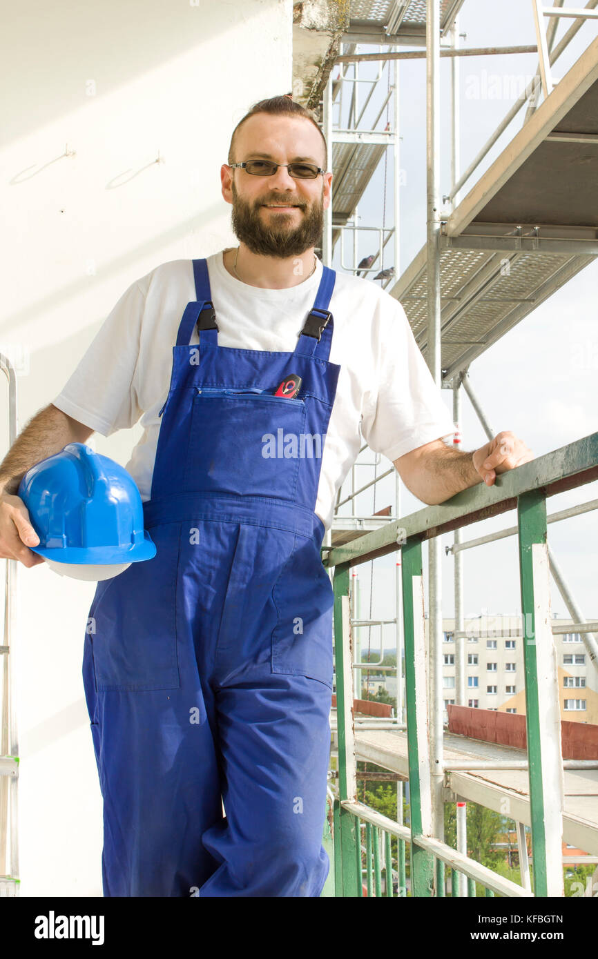 Lächelnd Bauarbeiter steht mit einem Schutzhelm in der Hand vor dem Hintergrund der Gerüste Stockfoto