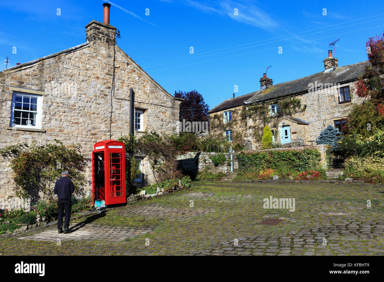 Aus Stein gebaute Häuser im Dorf von Healaugh Richmond ein Mensch, der einen traditionellen roten Britischen Telefonzelle NorthYorkshire England Stockfoto
