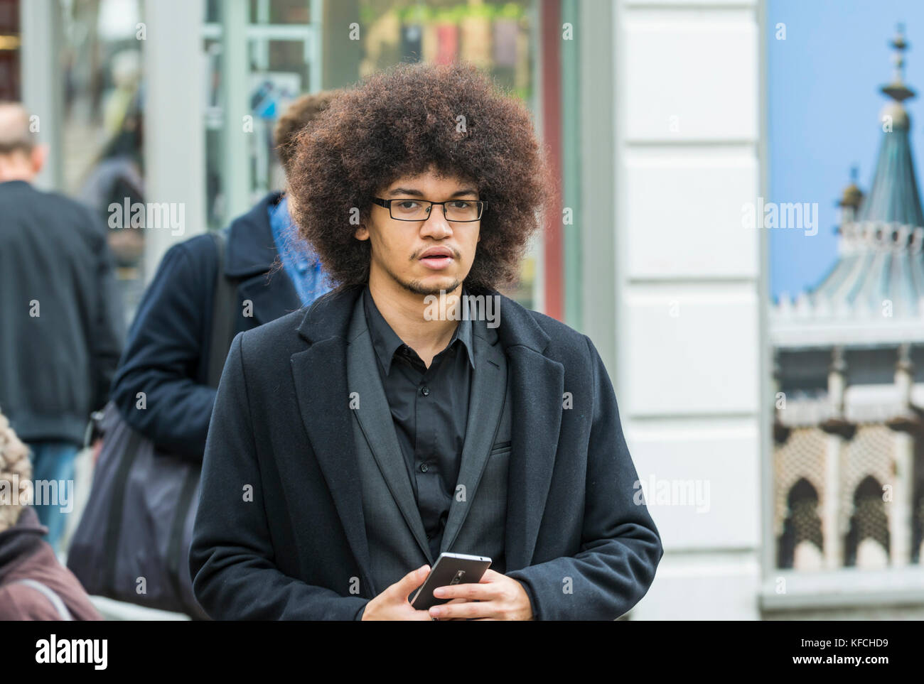 Junger Mann mit einem afro Frisur zu Fuß in einer Stadt in Brighton, East Sussex, England, UK. Stockfoto