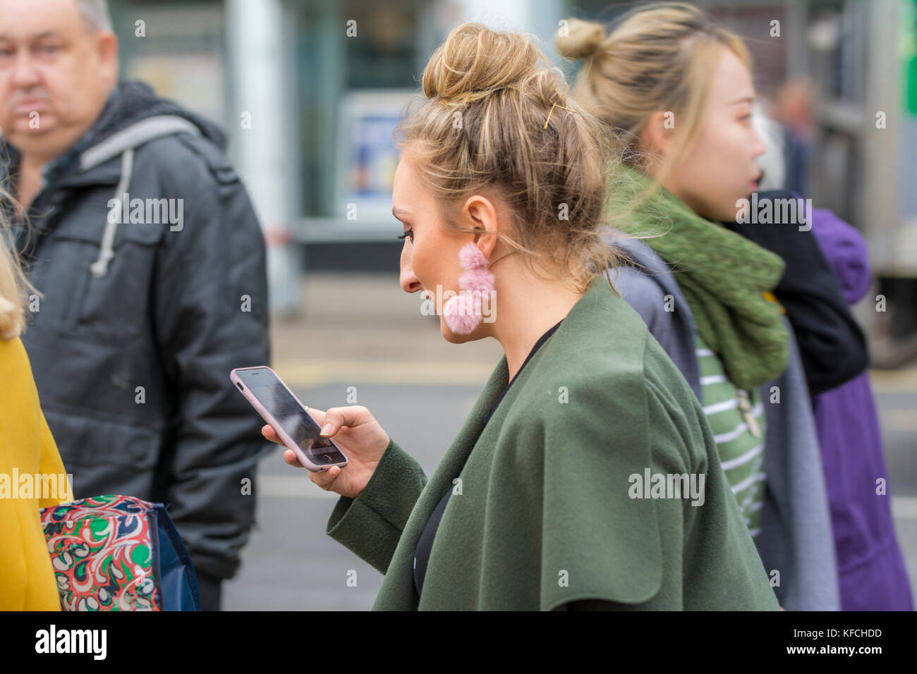 Junge Frau in einer geschäftigen Stadt zu Fuß, während Sie auf der Suche nach einem Smartphone in Brighton, East Sussex, England, UK. Stockfoto