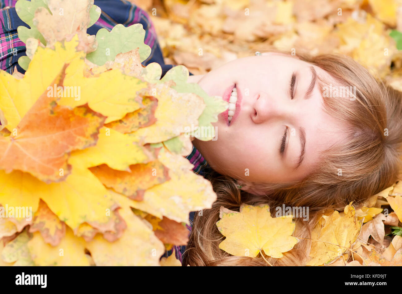 Eine nette junge Mädchen liegt auf Herbst Laub mit geschlossenen Augen, ein Bouquet von gelben Blätter im Herbst in den Händen Stockfoto