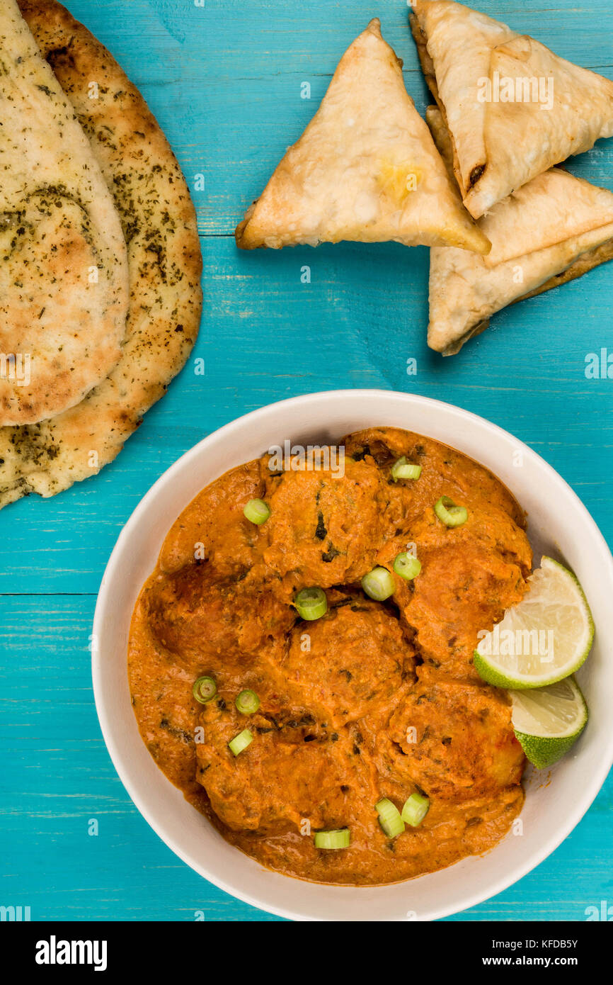 Im indischen Stil vegetable kofta Curry essen auf einem blauen Hintergrund aus Holz mit Naan Brot und Samosas Stockfoto