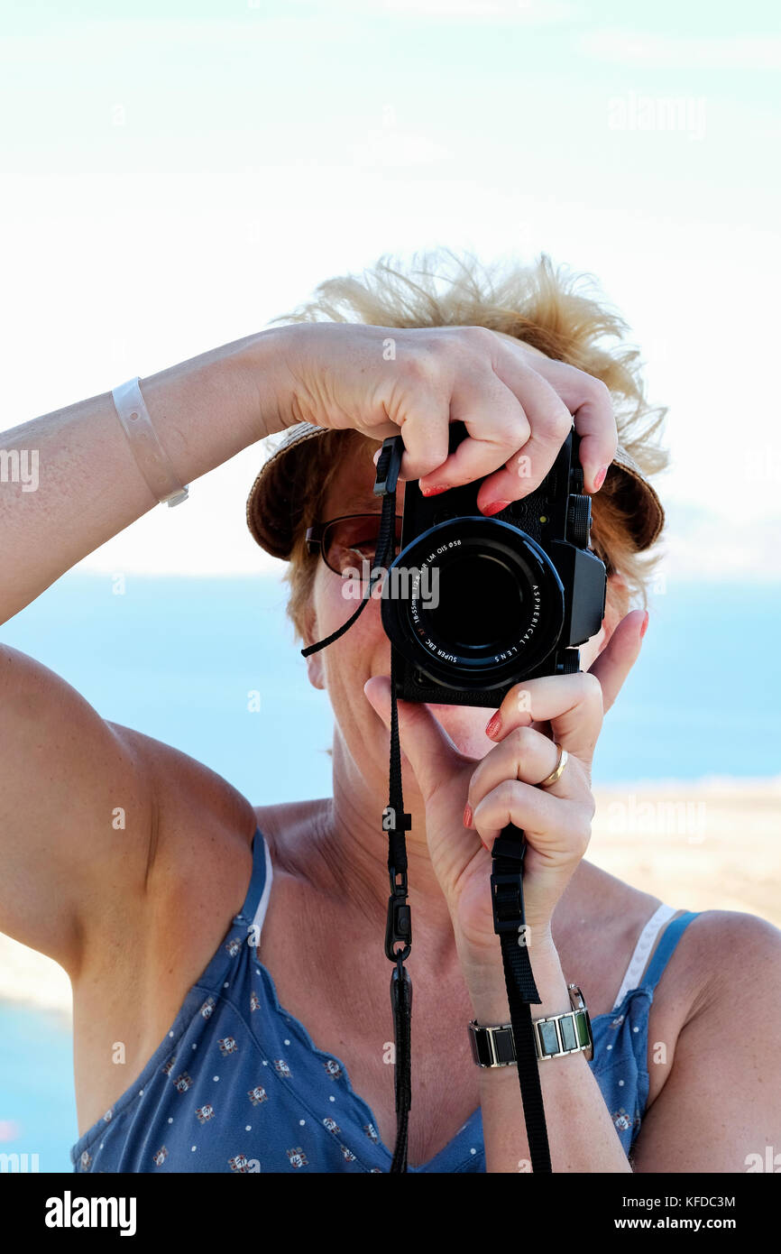 Eine Frau mittleren Alters, die eine spiegellose Kamera hochhält, um ein Bild aufzunehmen, und ihre Aufnahme mithilfe des Kamerasichtfinders zusammenstellt Stockfoto