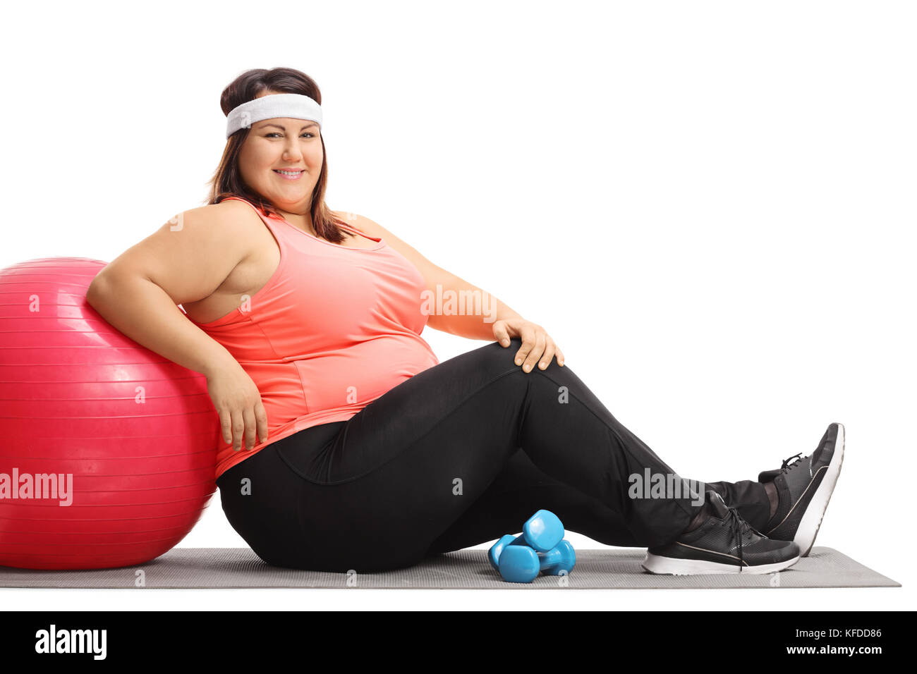 Übergewichtige Frau sitzt auf einer übung Matte und lehnte sich auf einem Pilates Ball auf weißem Hintergrund Stockfoto
