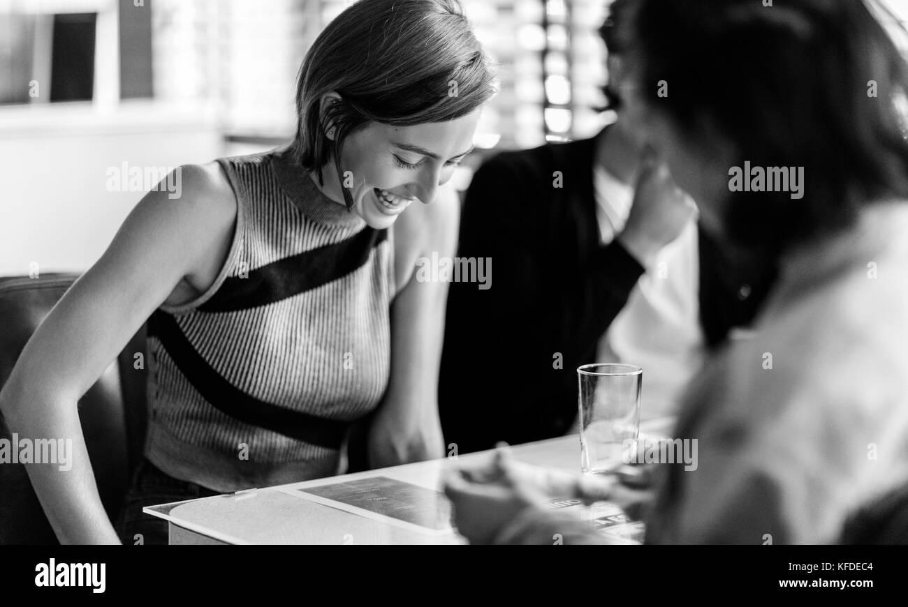 Lächelnde Frau saß mit zwei Freunden in einem Stand in einem Diner, blickte nach unten. Stockfoto