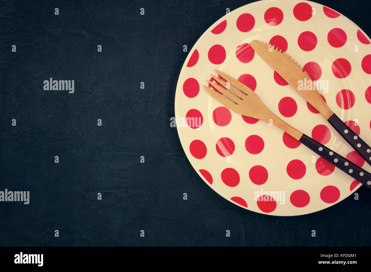 Retro Tisch mit einem Bambus Messer, Gabel und Teller mit Polka Dots auf einem dunklen Hintergrund Stockfoto