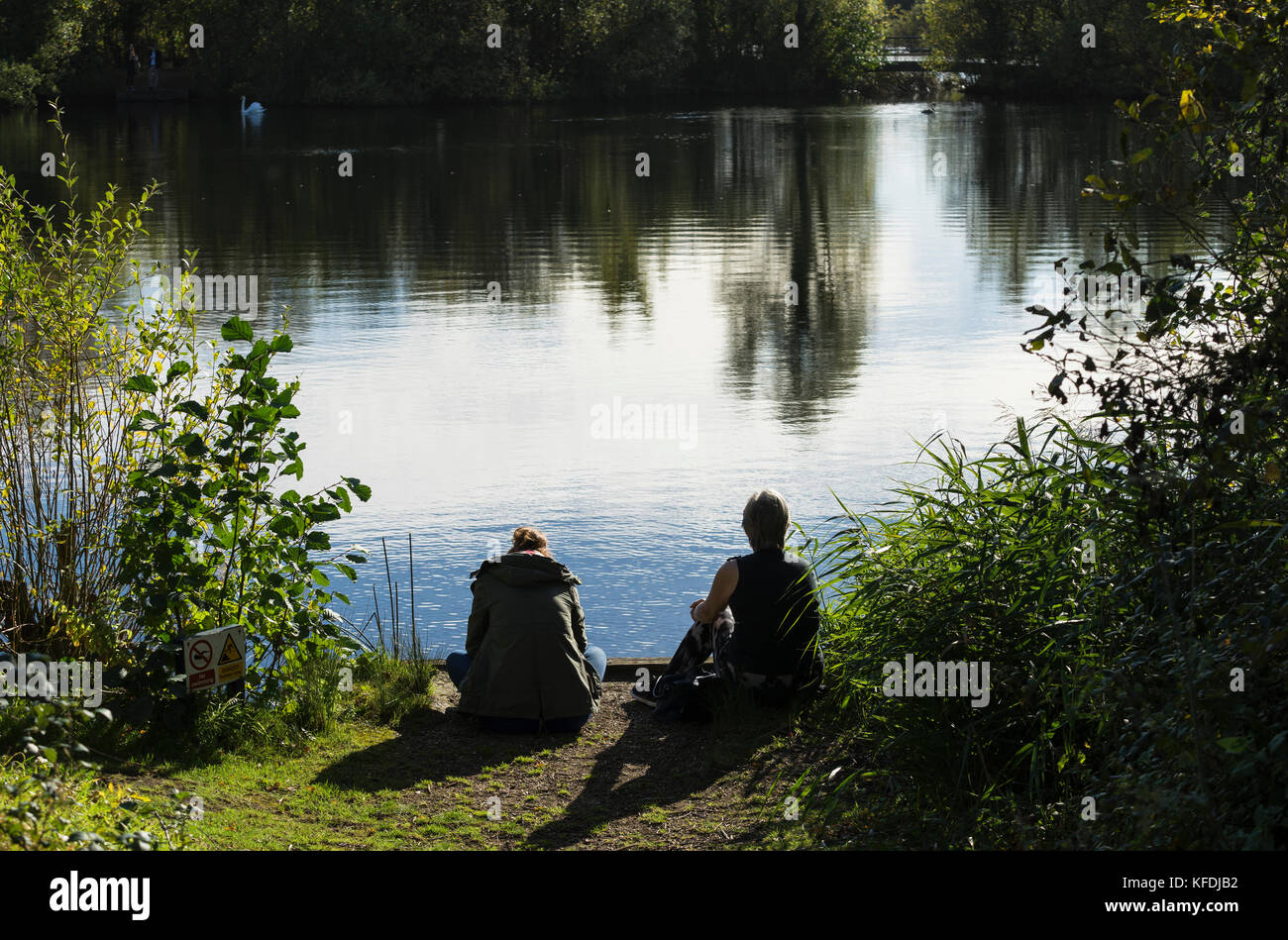 Zwei Damen setzte sich an einem See in der warmen Herbstsonne Stockfoto