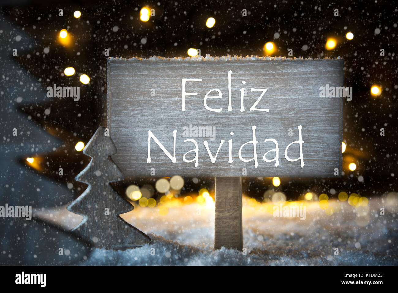 Schild mit der spanische Text Feliz Navidad, frohe Weihnachten. weißer Weihnachtsbaum mit Schnee und Magic glühenden Lichter im Hintergrund und Schneeflocken. Stockfoto