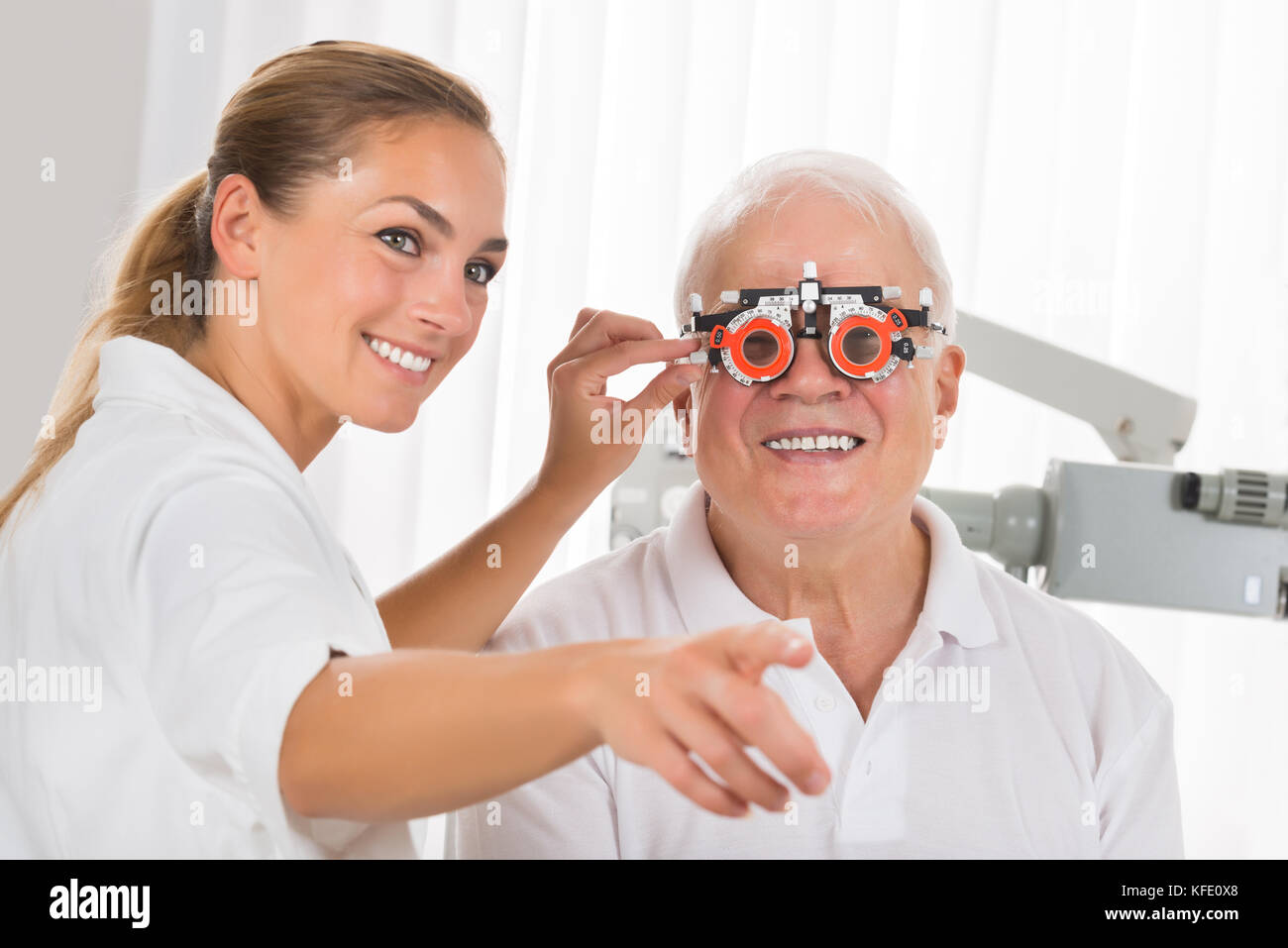 Lächelnde junge weibliche Optometriker prüfen die Vision der älteren männlichen Patienten mit Trial Rahmen Stockfoto Lächelnde junge weibliche Optometriker prüfen die Vision der älteren männlichen Patienten mit Trial Rahmen Stockfoto