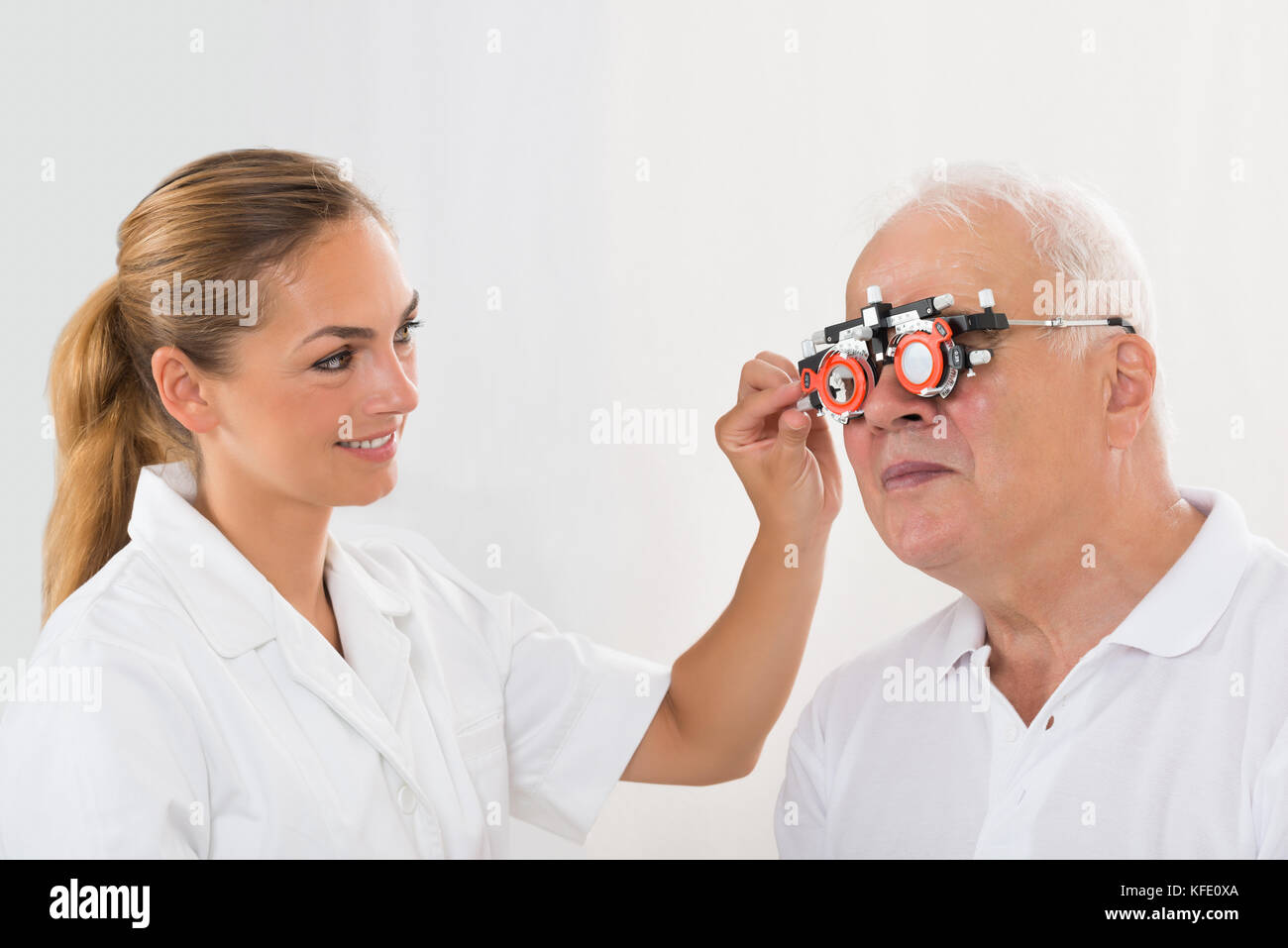 Lächelnde junge weibliche Optometriker prüfen die Vision der älteren männlichen Patienten mit Trial Rahmen Stockfoto Lächelnde junge weibliche Optometriker prüfen die Vision der älteren männlichen Patienten mit Trial Rahmen Stockfoto