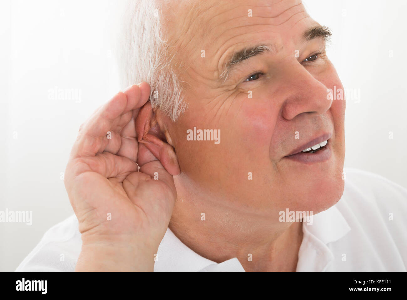 Älterer Mann, der versucht, mit der Hand über Ohrhörer zu hören Stockfoto