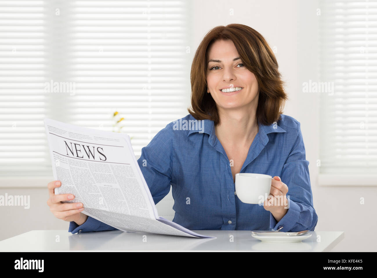 Junge Frau mit Tasse Kaffee und Zeitung Stockfoto