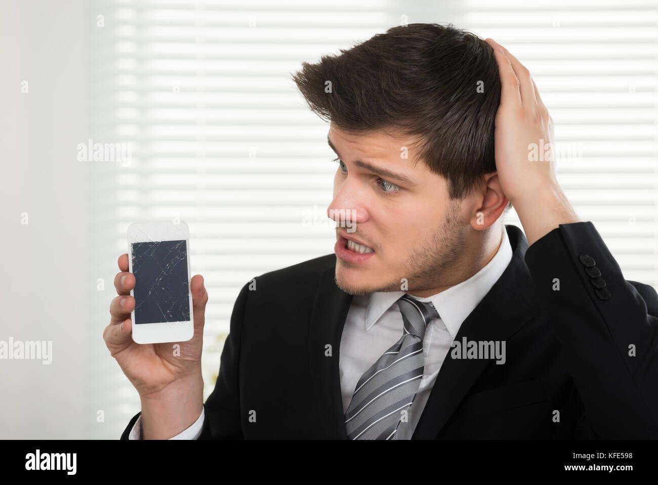 Unglückliche junge Unternehmer an defektem Handy suchen im Büro Stockfoto