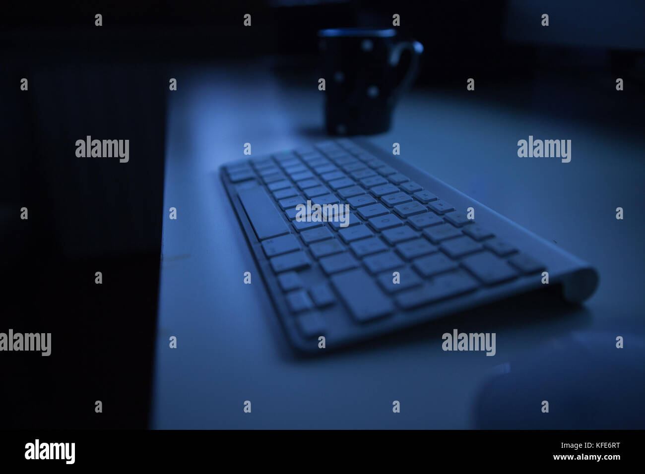 Drahtlose Tastatur auf einem Schreibtisch mit einer Tasse Tee oder Kaffee. Nachtlicht Stockfoto