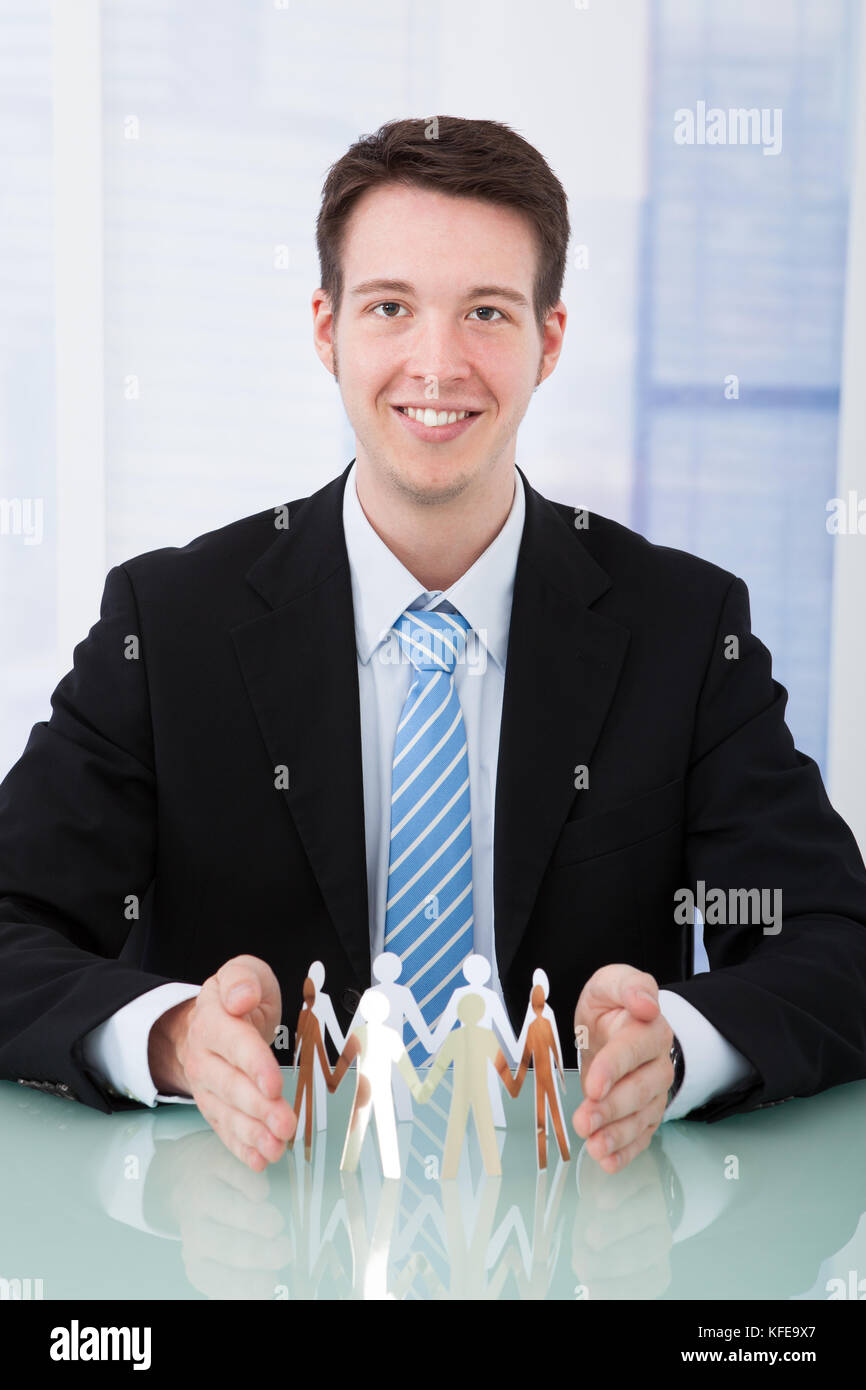 Portrait von selbstbewussten jungen Geschäftsmann Schutz team von Papier Menschen im Büro Schreibtisch Stockfoto