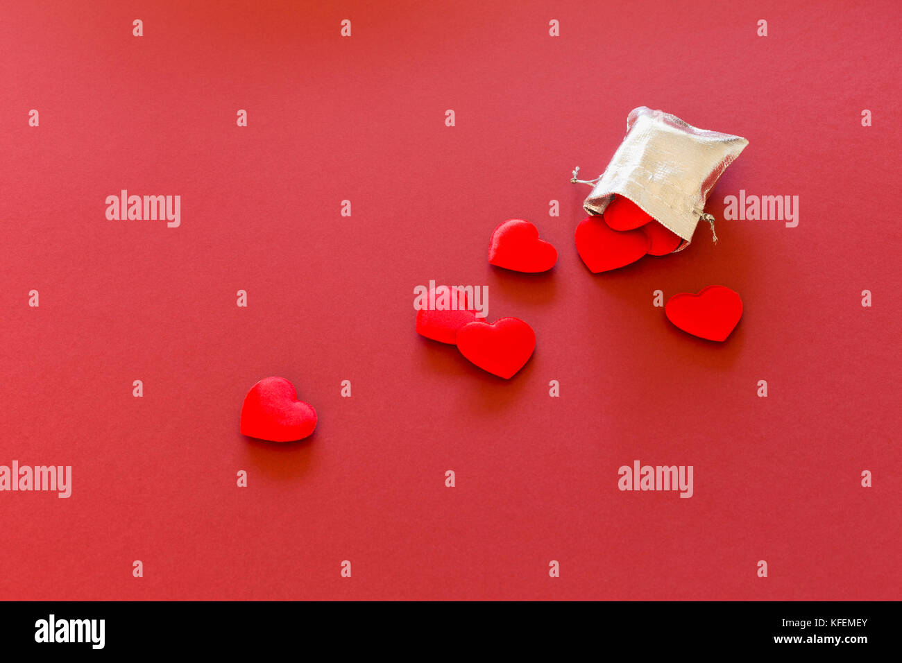 Nahaufnahme eines kleinen Glänzendes Silber Tasche mit niedlichen roten Samt Herzen auf rotem Hintergrund gefüllt. Konzept der romantischen Liebe Geschenk für Paare, Valentines Tag Stockfoto