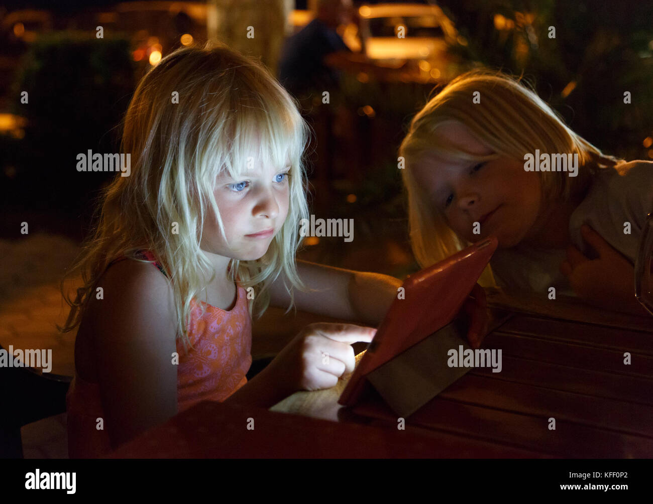 Mädchen Tippen auf das Ipad hier draussen auf ein Restaurant in Abend, wenn dunkel. Hier Gesicht leuchtet durch den Bildschirm. Ihr Freund ist auf der Suche interessiert was ist Goin Stockfoto