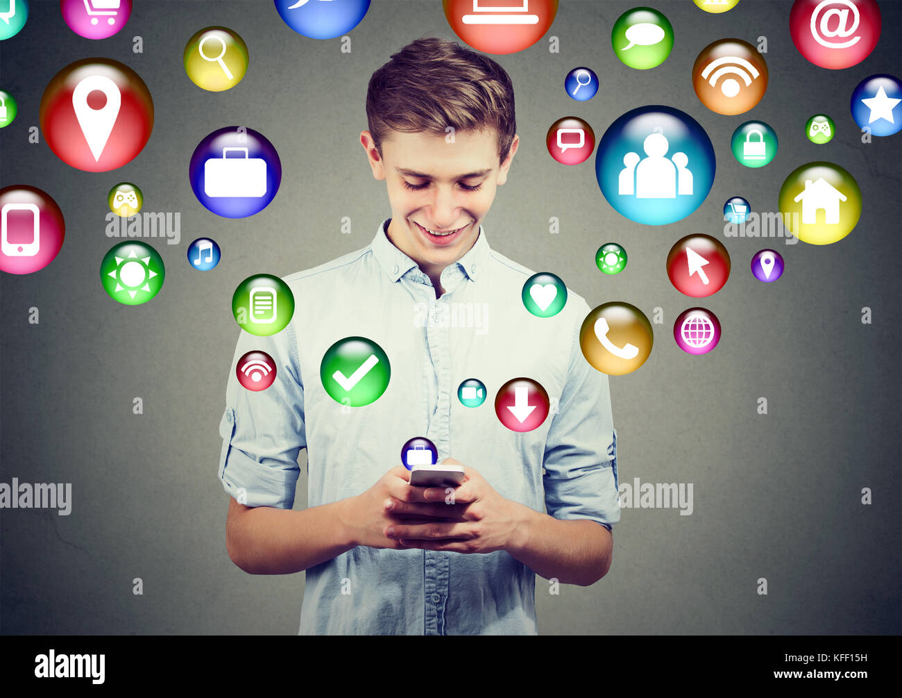 Mobile Technologie High-Tech-Konzept. Glückliche junge Mann mit smart phone mit social media Anwendungssymbole fliegen, der aus dem Bildschirm auf graue Wand isoliert Stockfoto