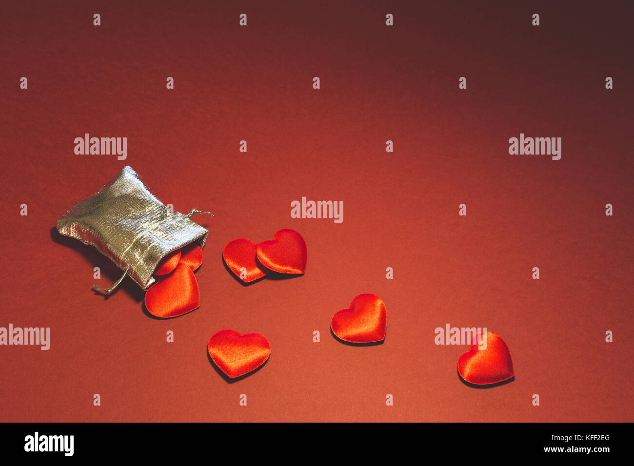 Nahaufnahme eines kleinen Glänzendes Silber Tasche mit niedlichen roten Samt Herzen auf rotem Hintergrund gefüllt. Konzept der romantischen Liebe Geschenk für Paare, Valentines Tag Stockfoto