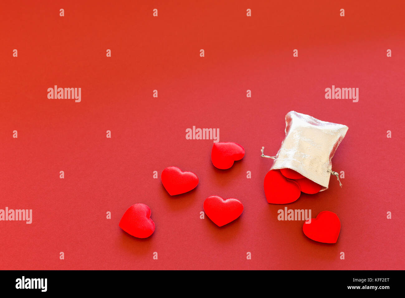 Nahaufnahme eines kleinen Glänzendes Silber Tasche mit niedlichen roten Samt Herzen auf rotem Hintergrund gefüllt. Konzept der romantischen Liebe Geschenk für Paare, Valentines Tag Stockfoto